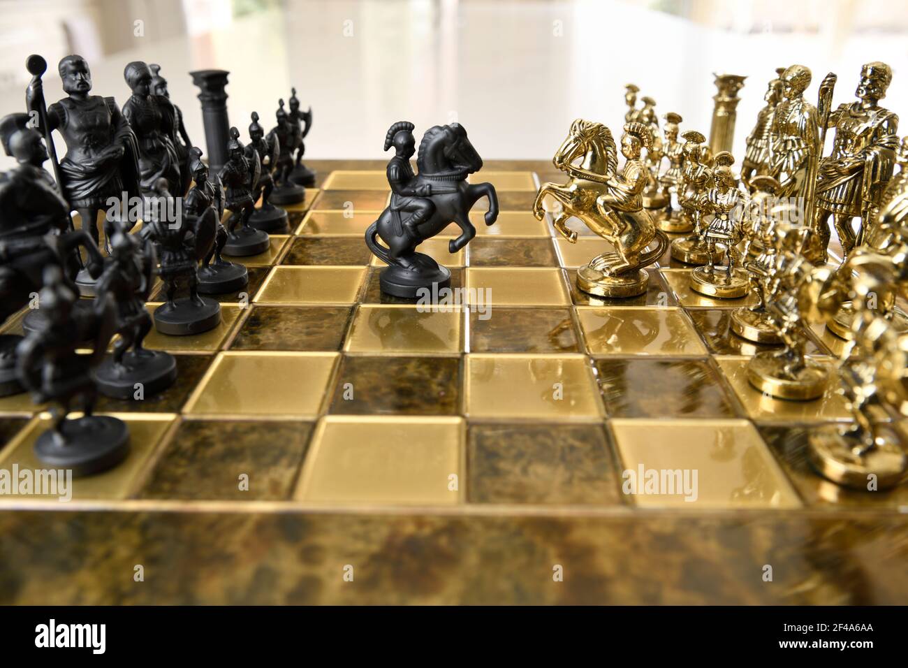 Black and gold metal knight chess figurines on horseback attacking on chessboard with opposing armies Stock Photo