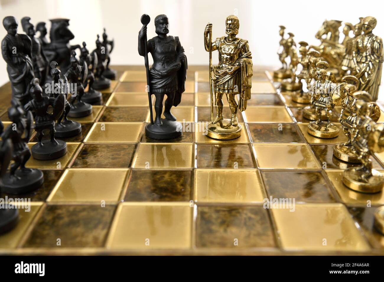 Black and gold metal Roman emperor King chess figurines from opposing armies on chessboard ready for battle Stock Photo