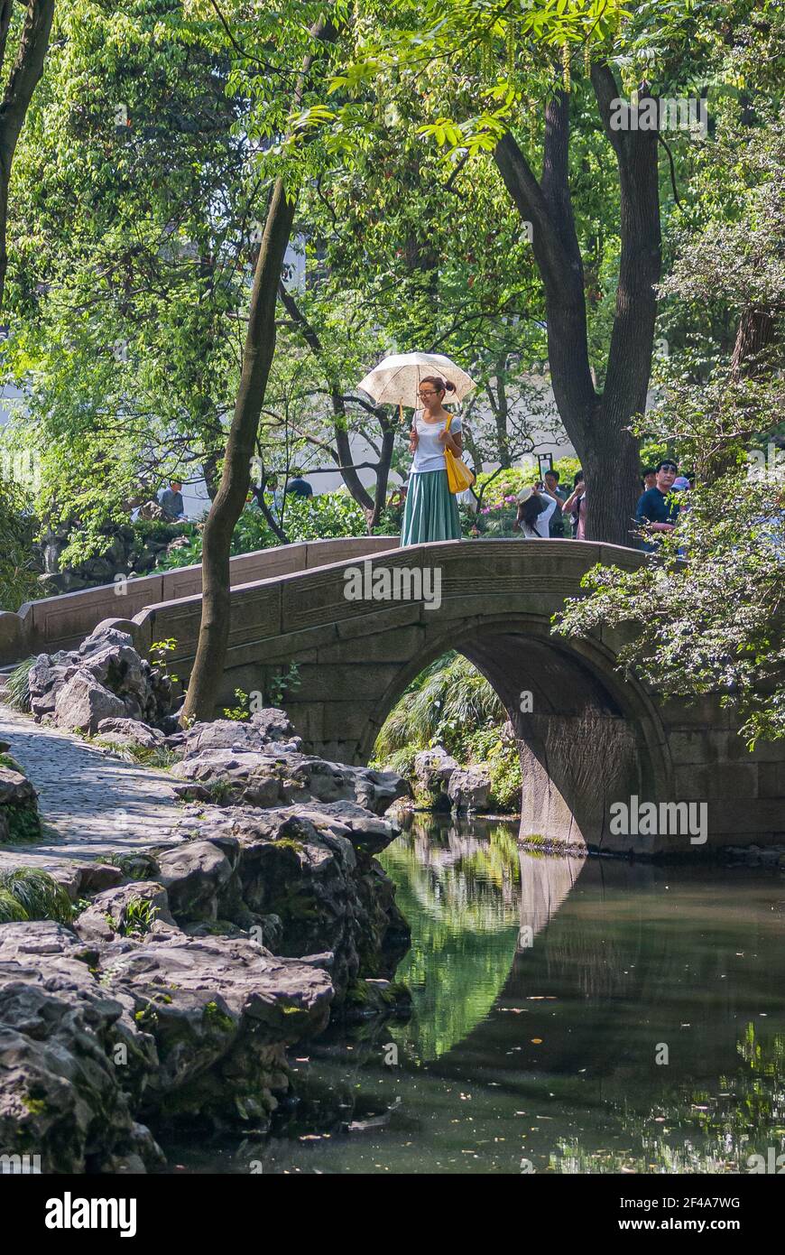 Suzhou, China - May 3, 2010: Humble Administrators Garden.  young woman with white umbrella stans on gray stone bridge over creek with rocky shore und Stock Photo