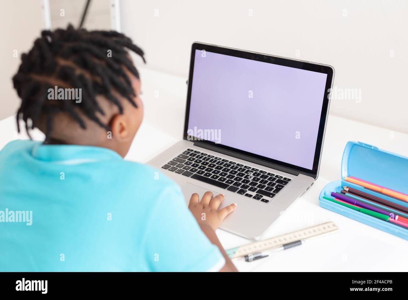 Rear view of african american boy at desk using laptop with copy space ...