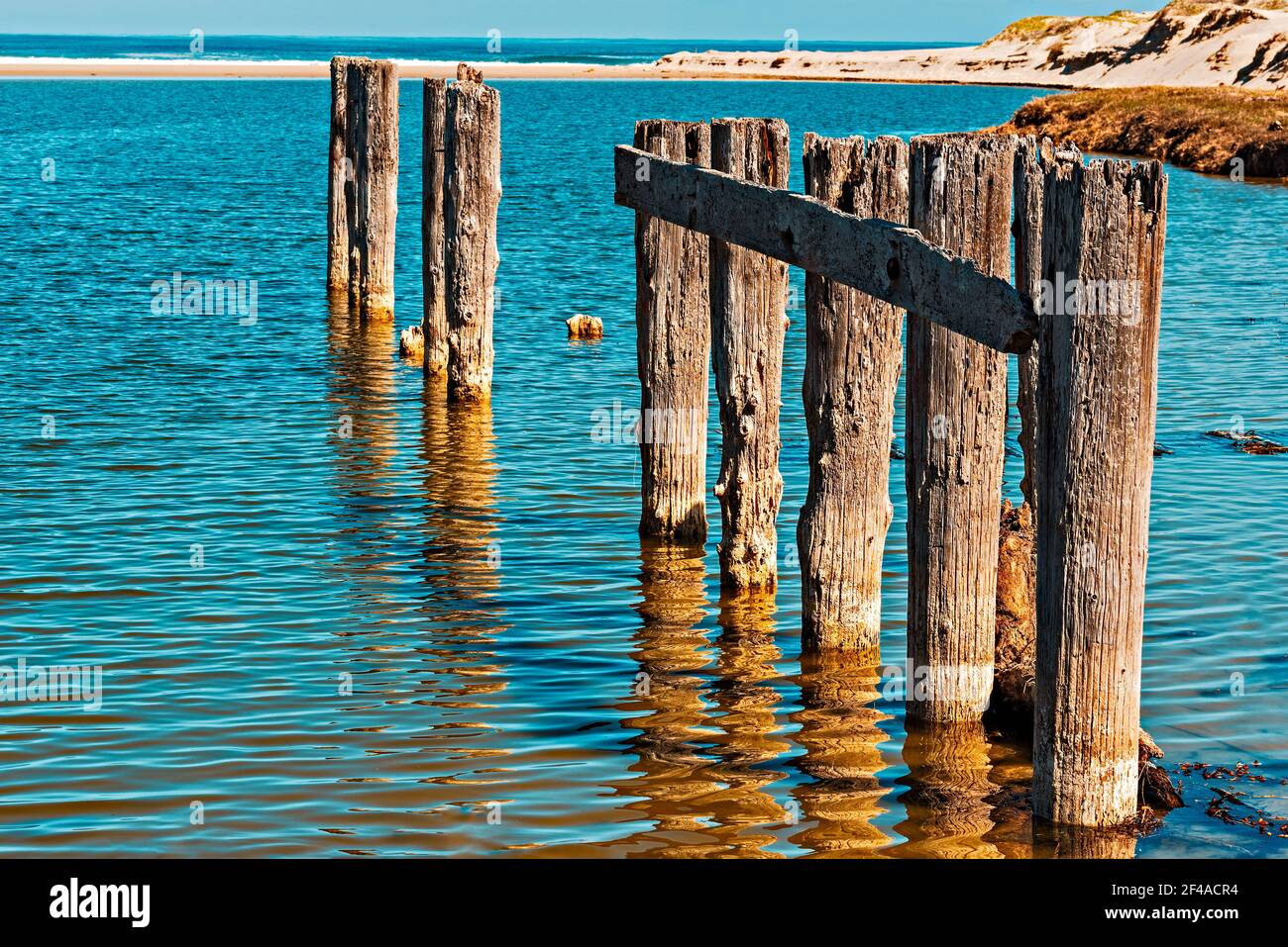 Remains of an old decaying pier in sea with beach beyond Stock Photo