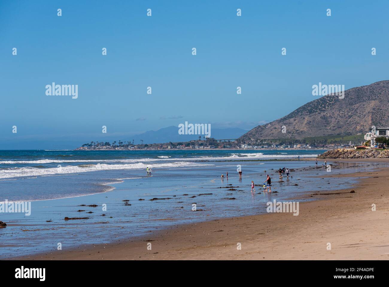 Sandy beach with tourists playing in the ocean, breaking waves and blue skies. Stock Photo