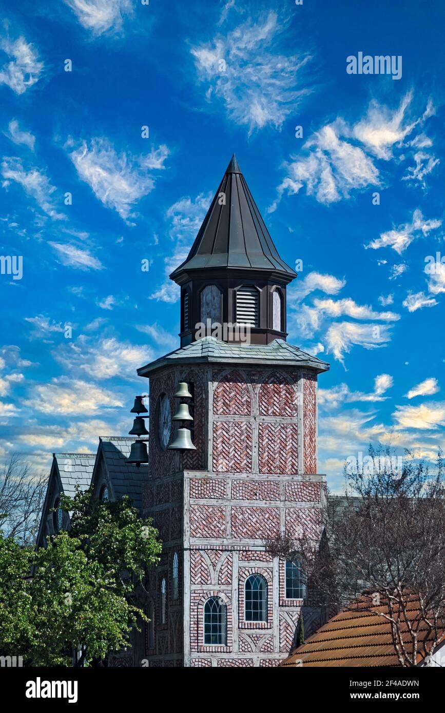 Tall brick building with belfry under blue skies with white fluffy clouds. Stock Photo