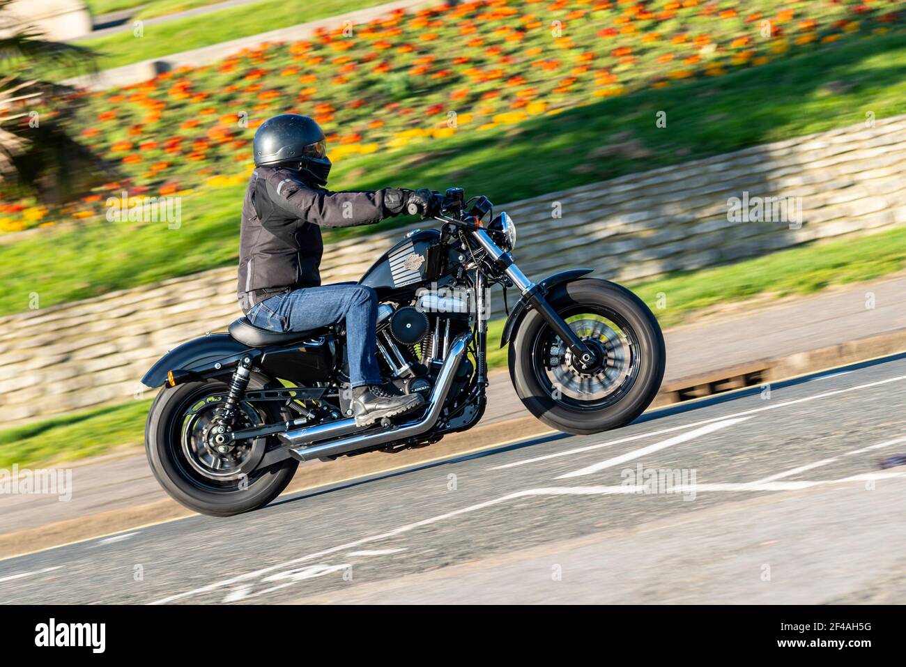 Harley Davidson Forty Eight motorcycle being ridden in Southend on Sea, Essex, UK on a bright sunny day, passing the Cliff Gardens Stock Photo
