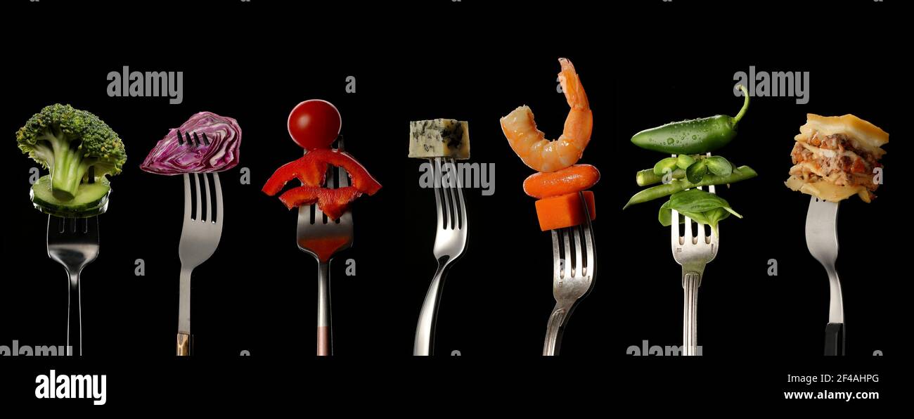 Different food impaled on forks against dark background Stock Photo