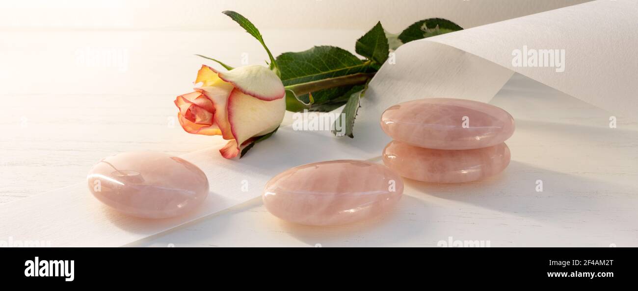 Rose quartz stones for cooling after wax depilation and massage, paper fleece and a rose flower on a light background, cosmetic treatment in panoramic Stock Photo