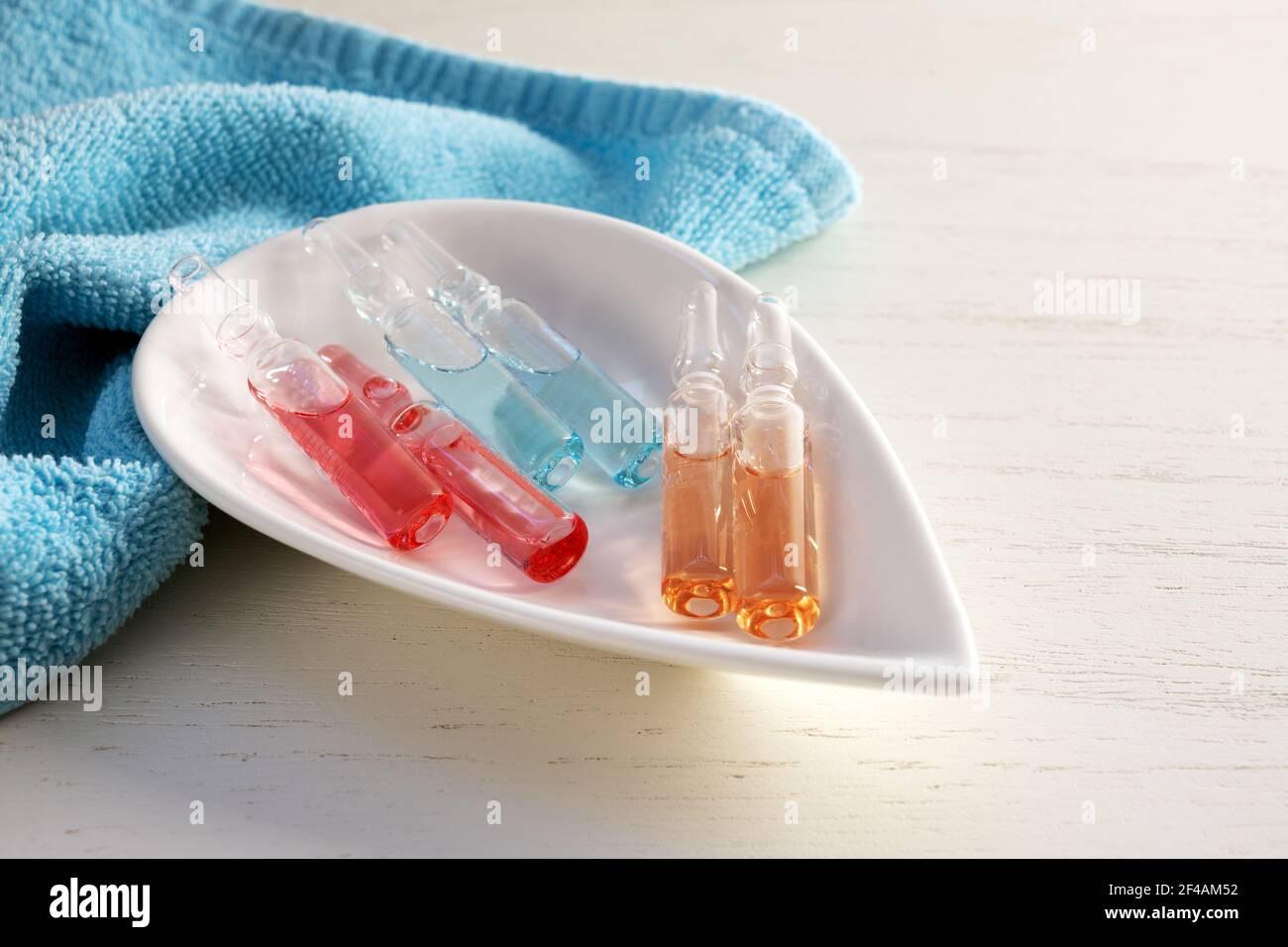 Colored glass ampoules for cosmetic beauty treatment in a bowl, blue towel and white wooden background, copy space, selected focus, narrow depth of fi Stock Photo