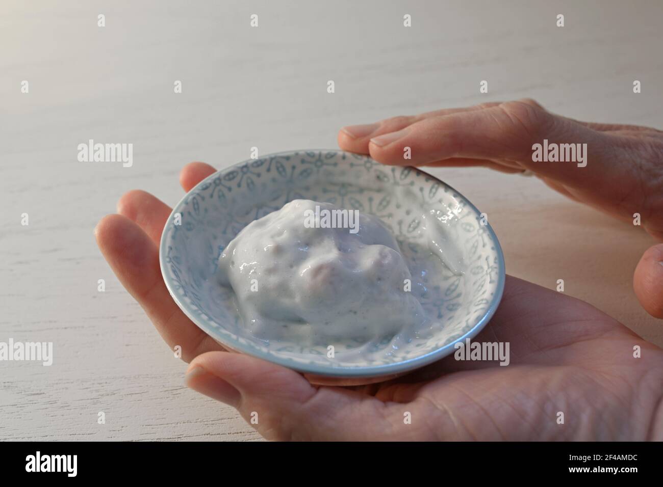 Female hands of a cosmetician holding a small bowl with mixed two component cream for a cosmetic skin treatment, copy space, selected focus, narrow de Stock Photo