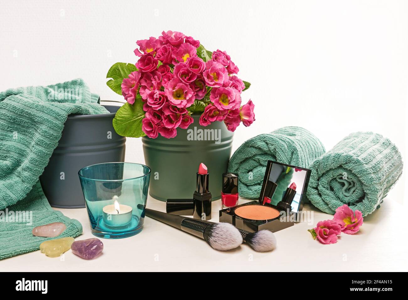 Arrangement of beauty and make-up utensils like lipstick, nail polish and face powder with cosmetic brushes, turquoise towels, candle and pink flowers Stock Photo