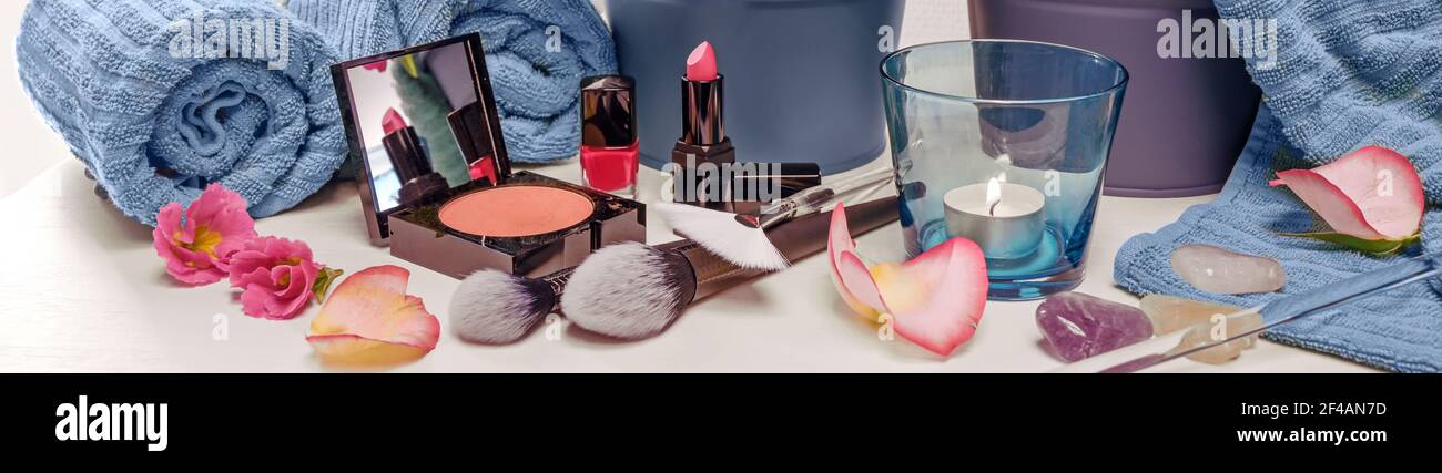 Make-up utensils like face powder, red pink lipstick and nail polish with cosmetic brushes, blue towels, candle and flower petals, panoramic banner fo Stock Photo