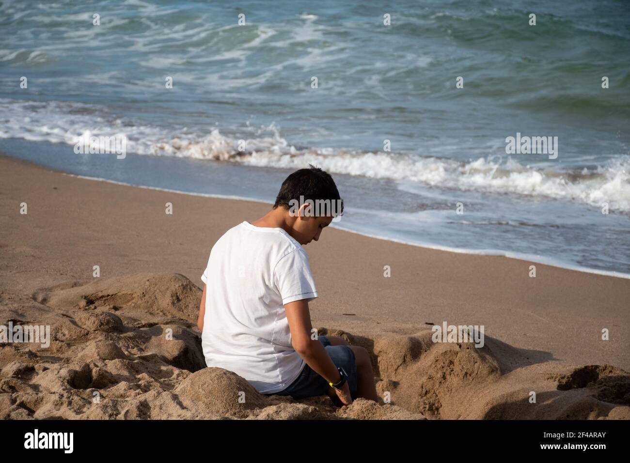 boy sitting on the sand on the beach inside a sand hole by the sea