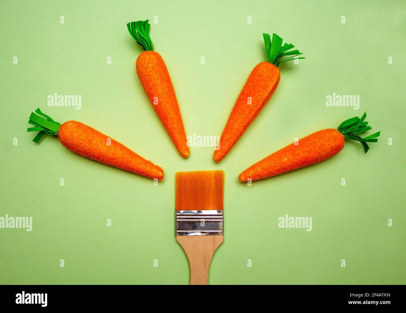 Four carrots with a paint brush on the bottom on green background. Easter, spring holidays concept Stock Photo
