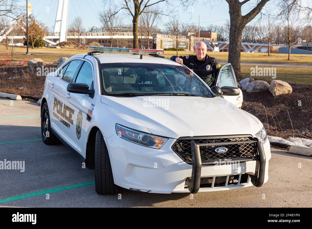 A Purdue University Fort Wayne police officer stands next to a white patrol car on campus. Stock Photo