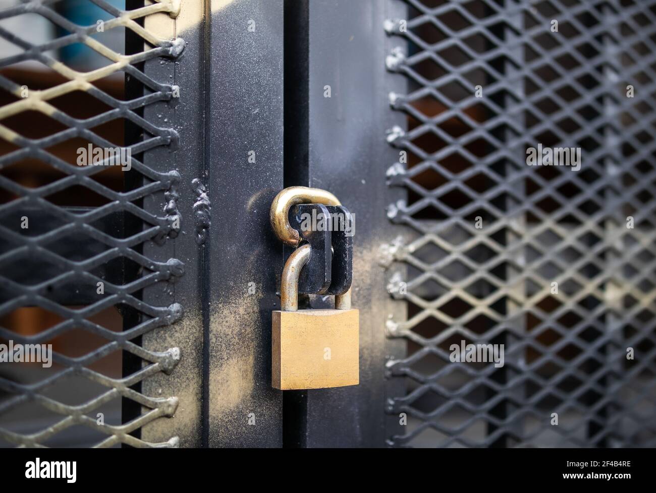 Padlock on outdoor door, close up. Caged in commercial or residential area. Golden metal lock on black fence with reinforced mesh and gold spray paint Stock Photo