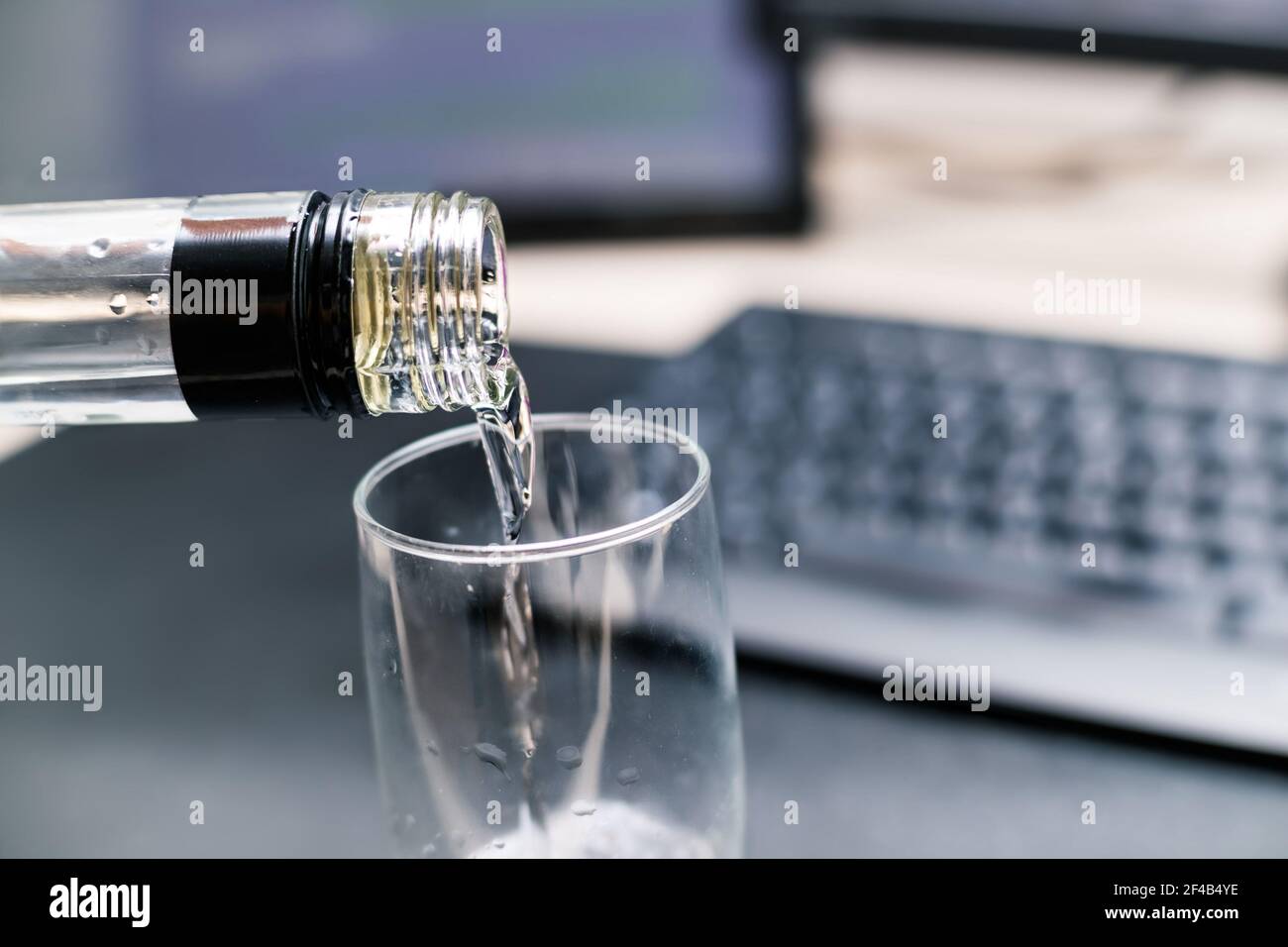 Drinking alcohol at work or office. Vodka is poured in a glass. Defocused keyboard and desk showing vision problems and drowsiness. Concept for how to Stock Photo