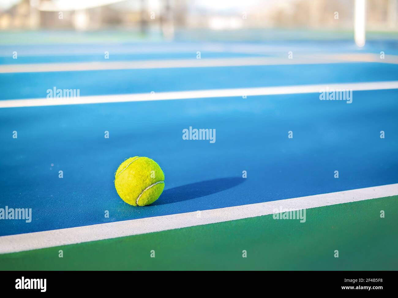 Yellow tennis ball next to sideline in outdoor tennis court, closeup. Defocused and abstract blue and green rubberized ground surface for shock absorp Stock Photo