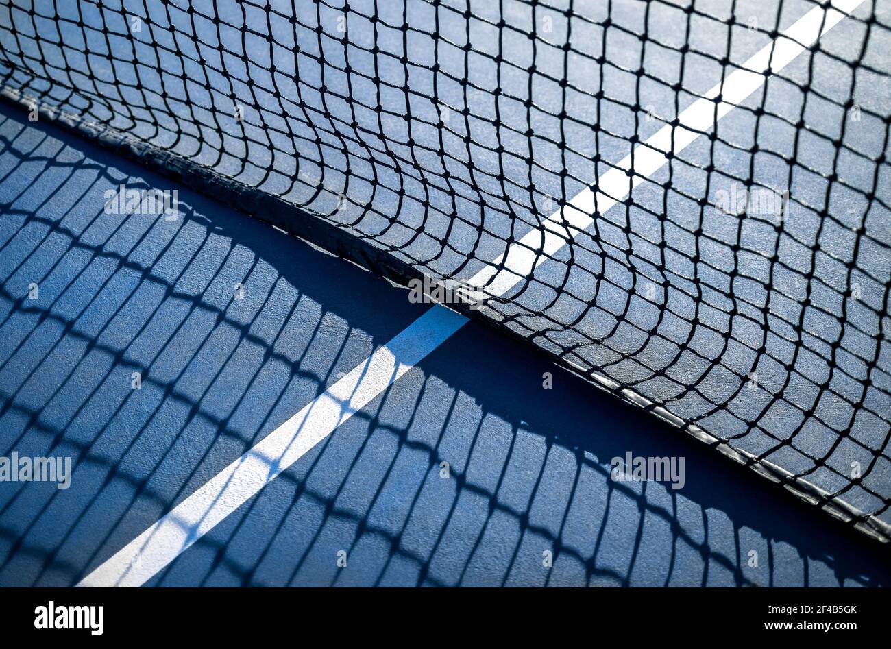 Abstract tennis court sport texture. Defocused perspective view of white center service line by the net, outside early morning. Blue rubberized and gr Stock Photo