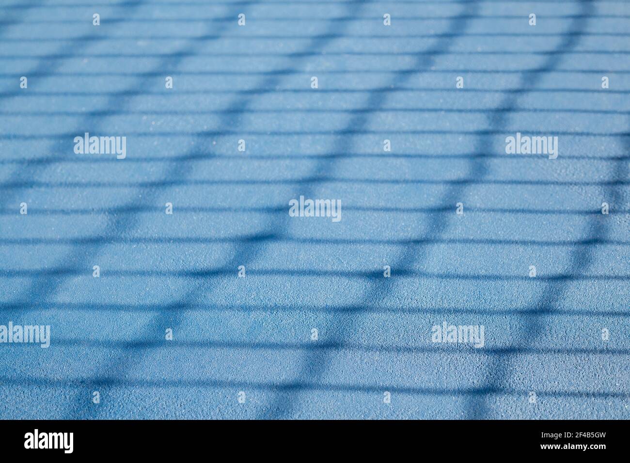 Abstract tennis court texture. Defocused tennis net shadow on ground, outside early morning. Blue rubberized and granulated ground surface for shock a Stock Photo