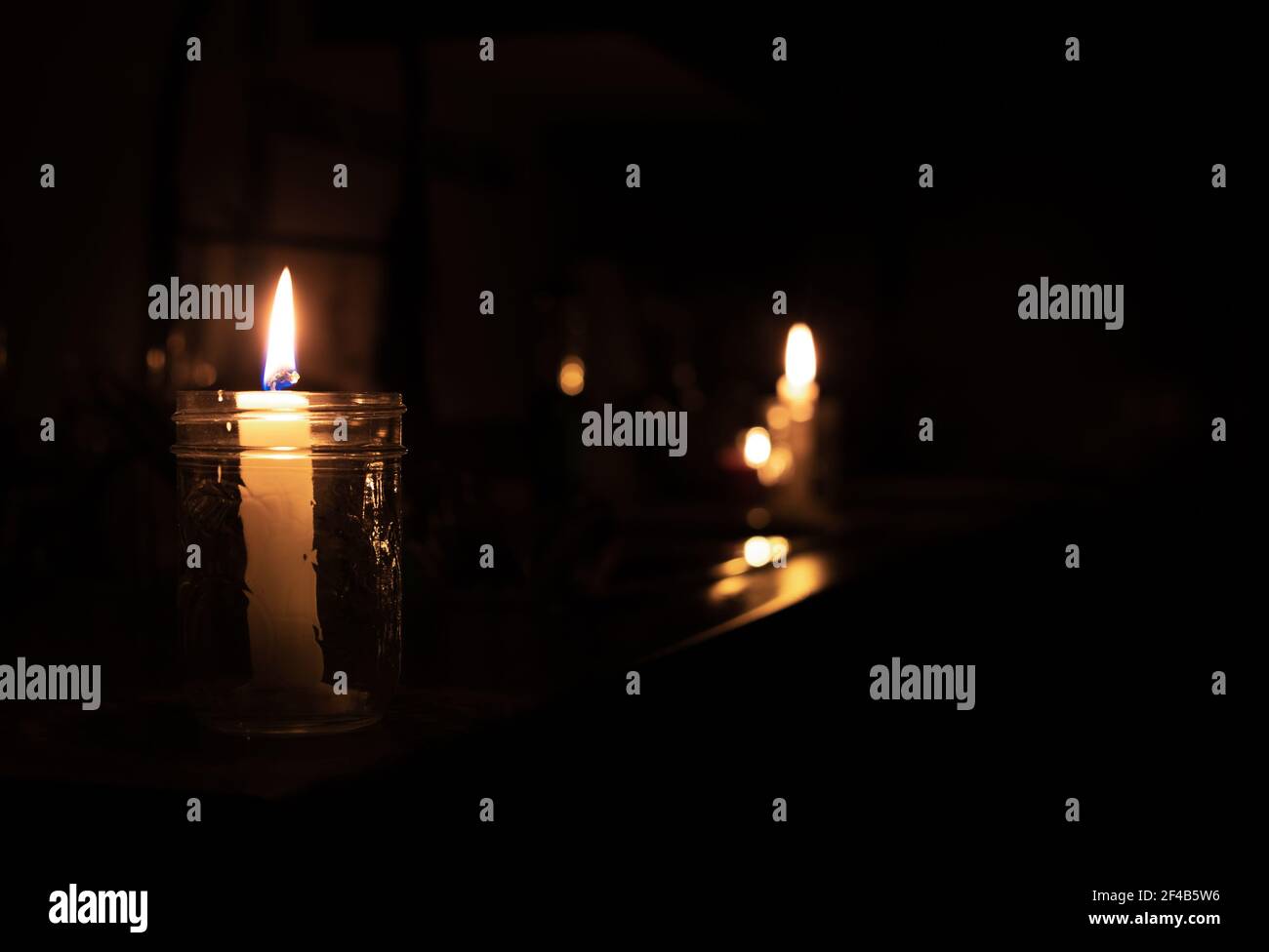 Candles on kitchen counter during power outage. 2 candles are inside a mason jar. Pitch black room except the candle lights. Selective focus on first Stock Photo