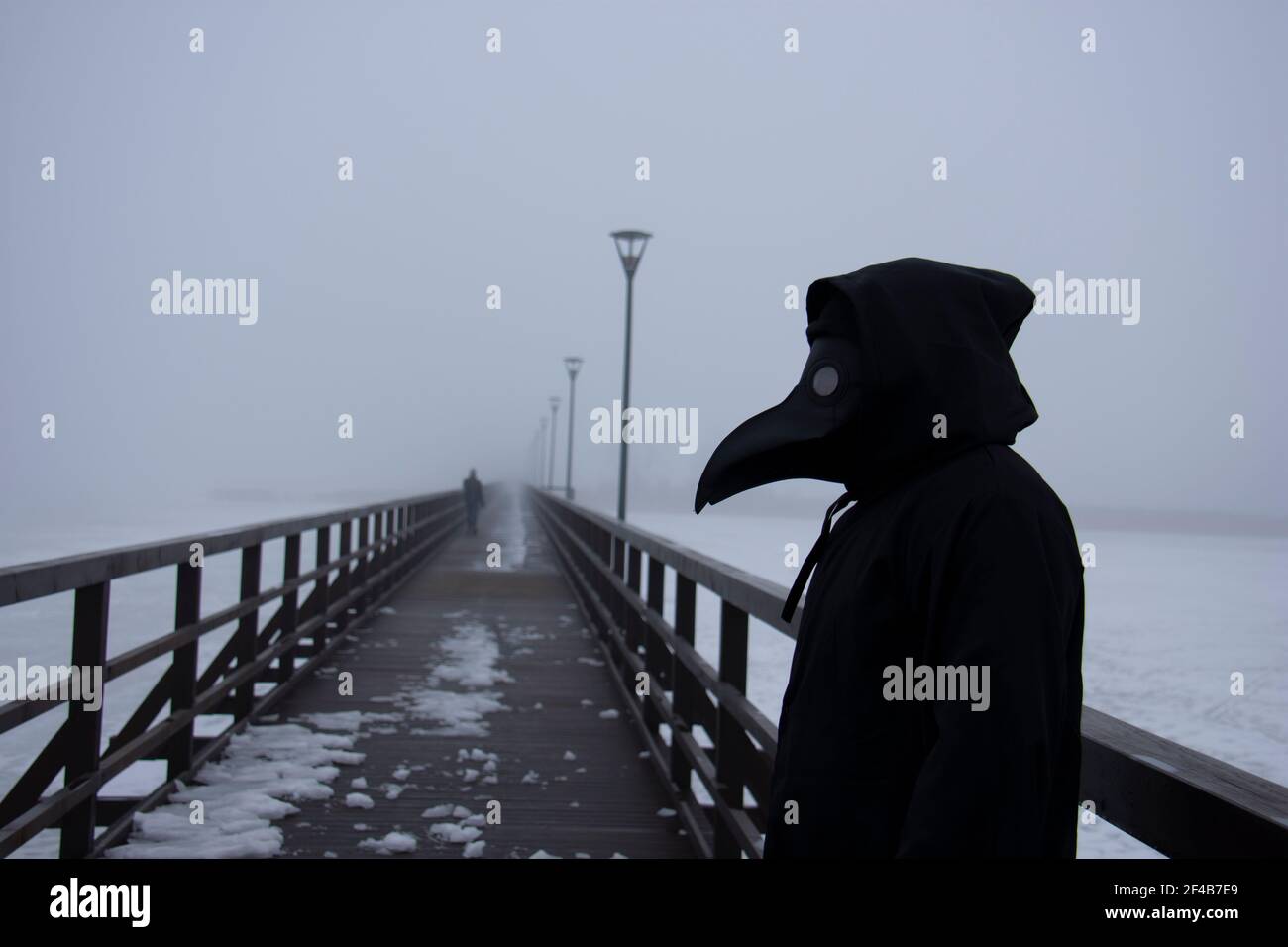 Medieval plague doctor stands on winter wooden bridge, pandemic symbol Stock Photo