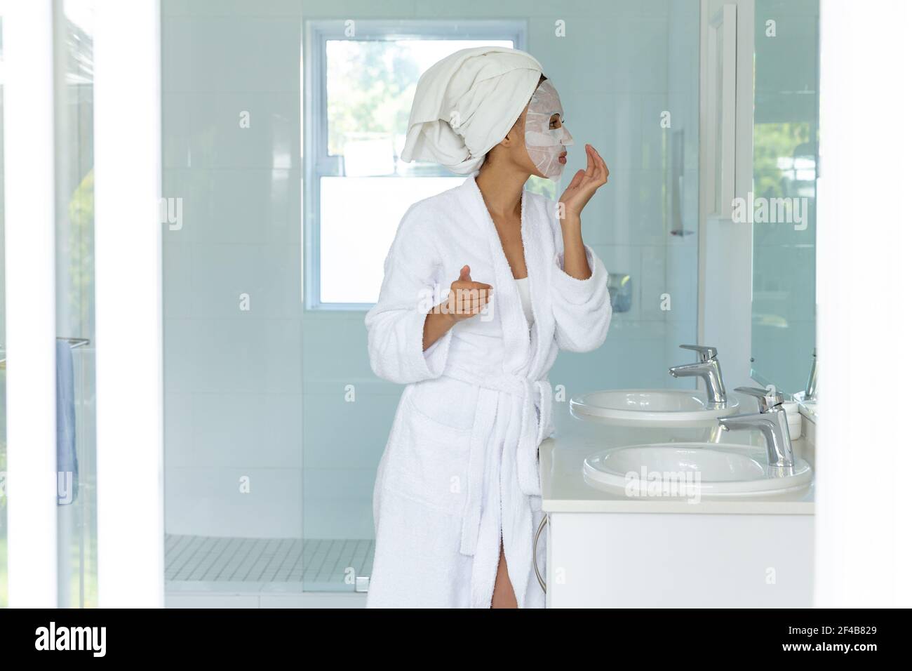 Mixed race woman wearing bathrobe and cleansing face mask in bathroom Stock Photo