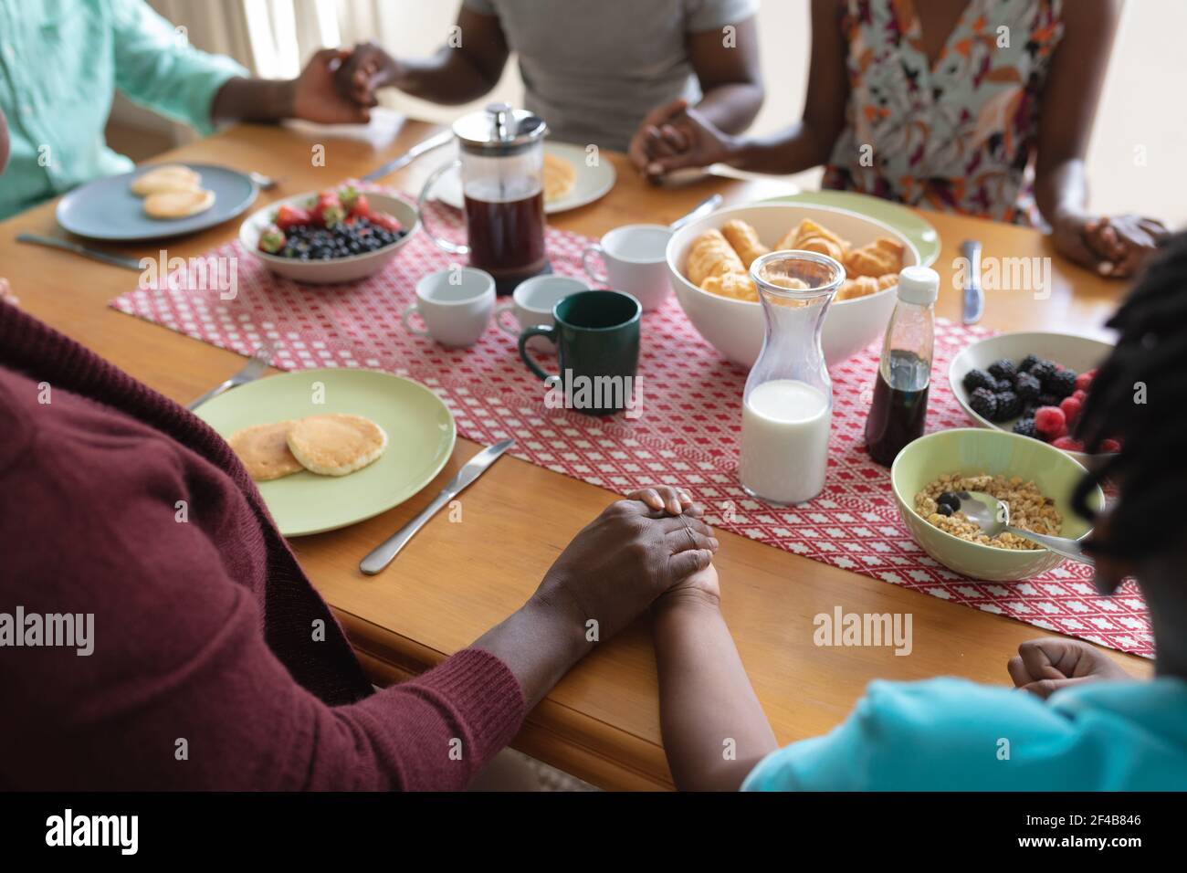 Midsection of african american parents, son and grandparents holding hands in prayer at dinner table Stock Photo