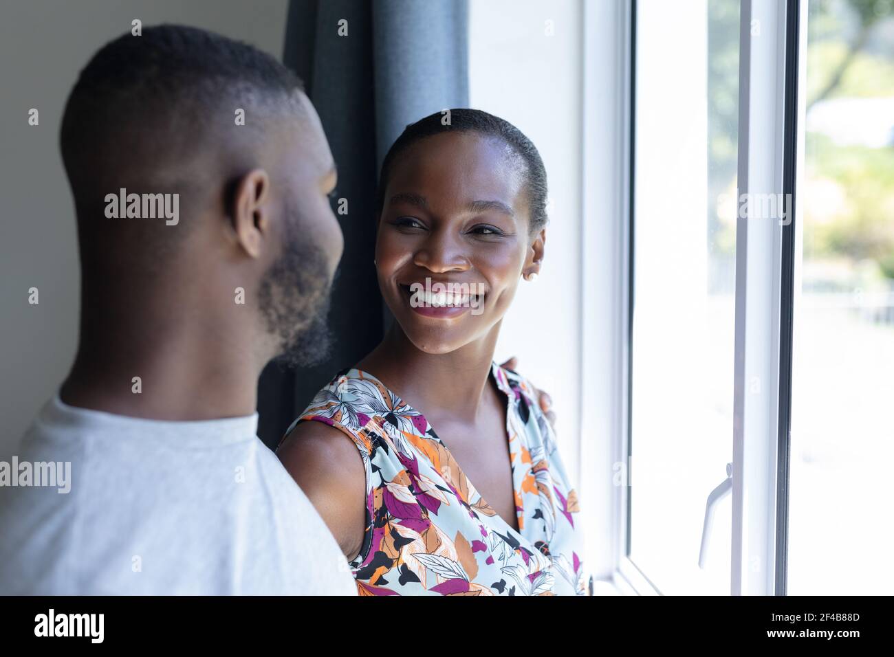 Happy african american couple standing by window looking at each other ...