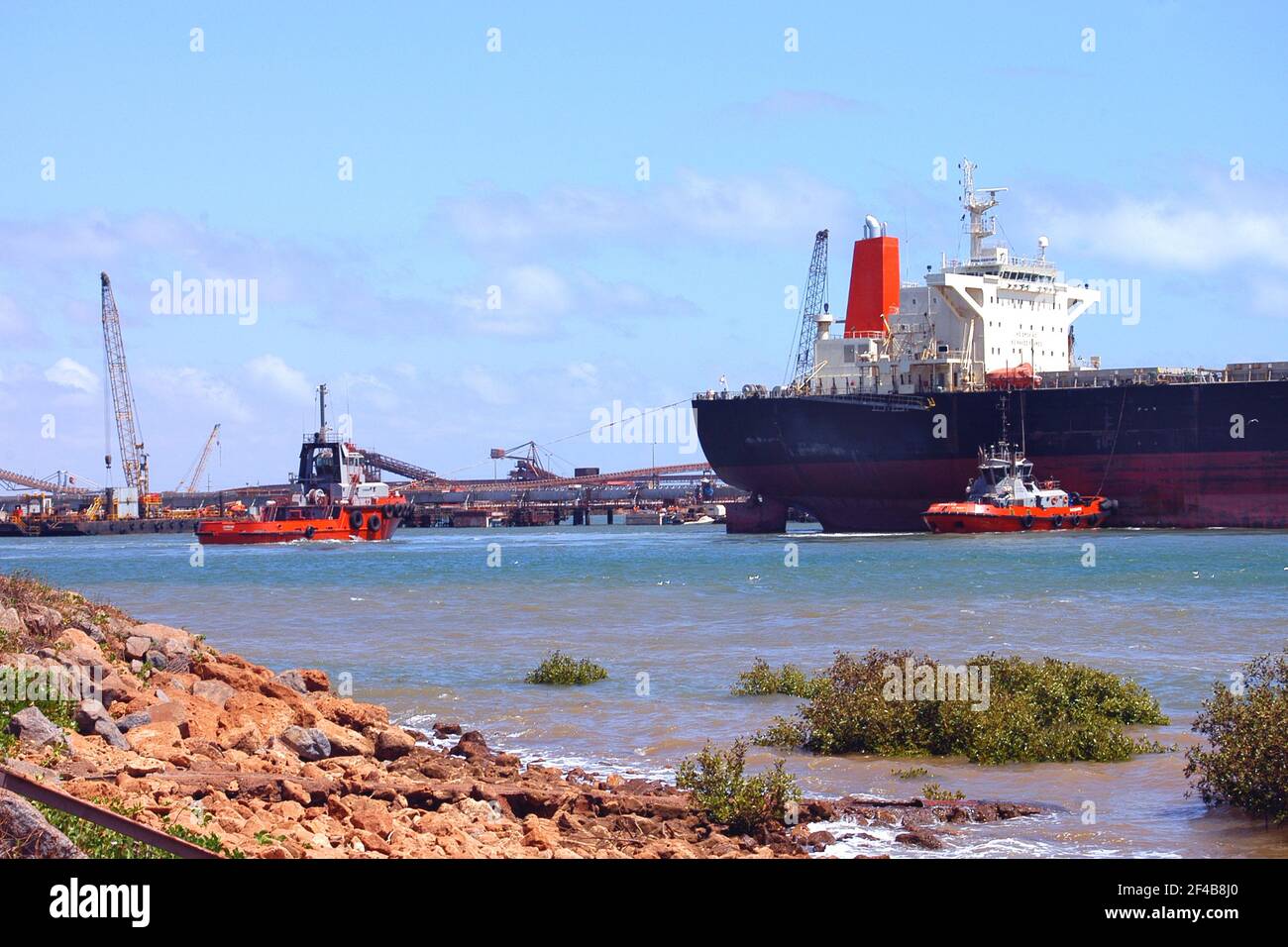 PORT HEDLAND HARBOUR. TUG BOATS GUIDE A LARGE CARGO SHIP INTO THE DOCK. PORT HEDLAND IS THE