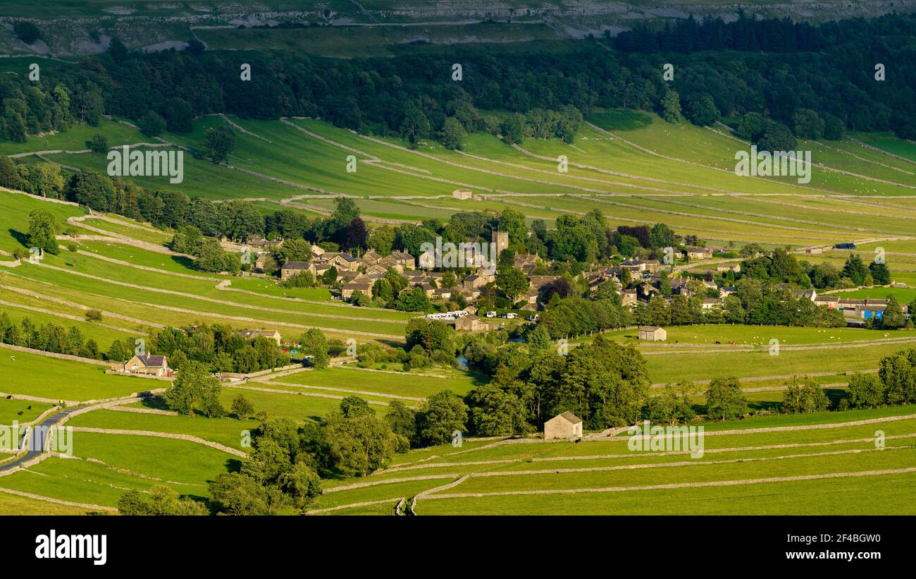 Picturesque Dales village (cottages & houses) nestling by steep hillside slope in wide sunlit u-shaped valley - Kettlewell, Yorkshire, England, UK. Stock Photo