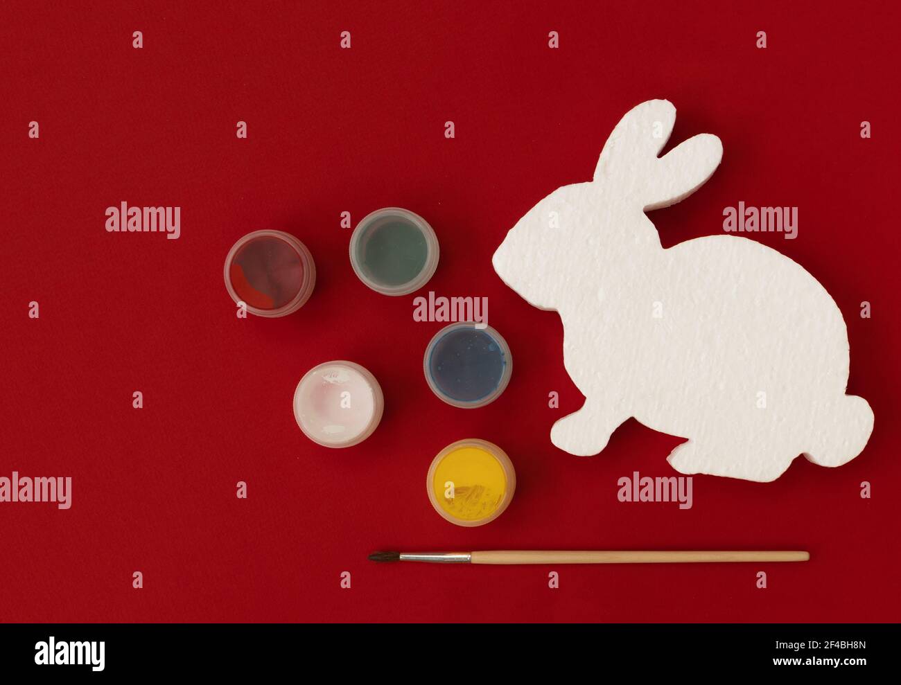 White figure of bunny or rabbit for decorating, paints and brushe on red background. Easter diy with children. Top view with copy space. Stock Photo