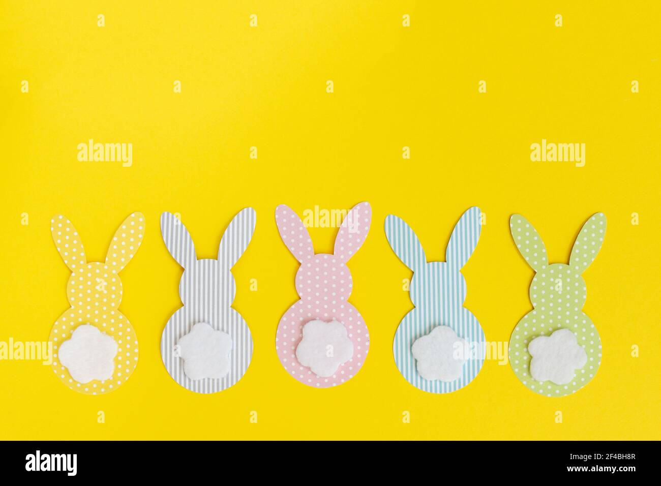 Easter paper bunnys isolated on yellow background. DIY holiday handicraft decoration of colorful rabbits. Concept: children's crafts for Easter. Top v Stock Photo