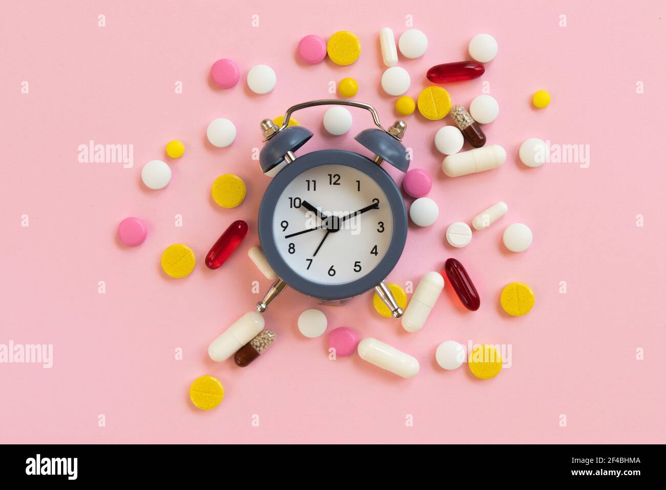 Many different pills with alarm clock on a pink background. Time to