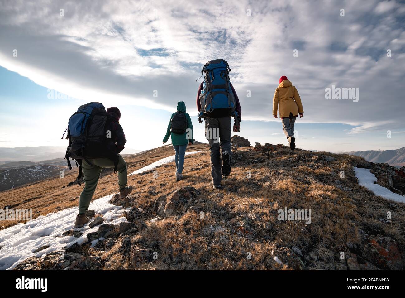 Group of four diverse tourists or hikers are walking on mountain top at sunset time Stock Photo