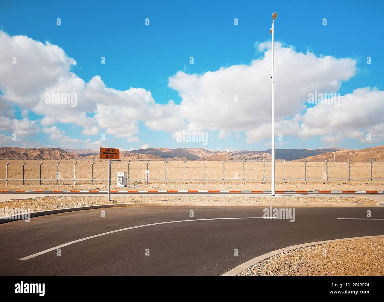 Empty road near Eilat airport parking lot with exit sign (English and Israeli translation), low mountains behind fence in distance Stock Photo