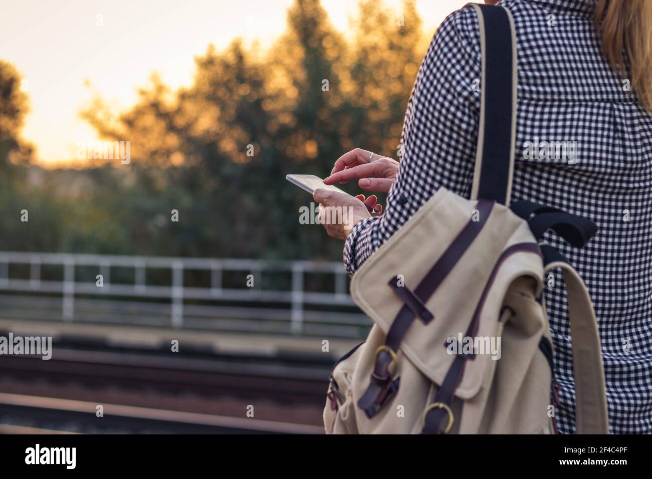 Woman using phone on railroad station. Traveler using smart phone during waiting for train. Stock Photo