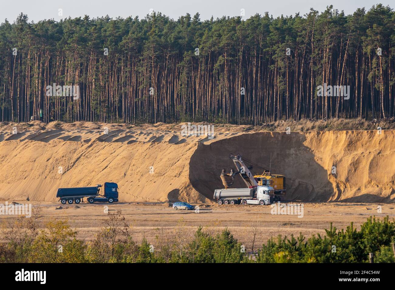 Heavy excavator and trucks in sand quarry, mining industry. Stock Photo