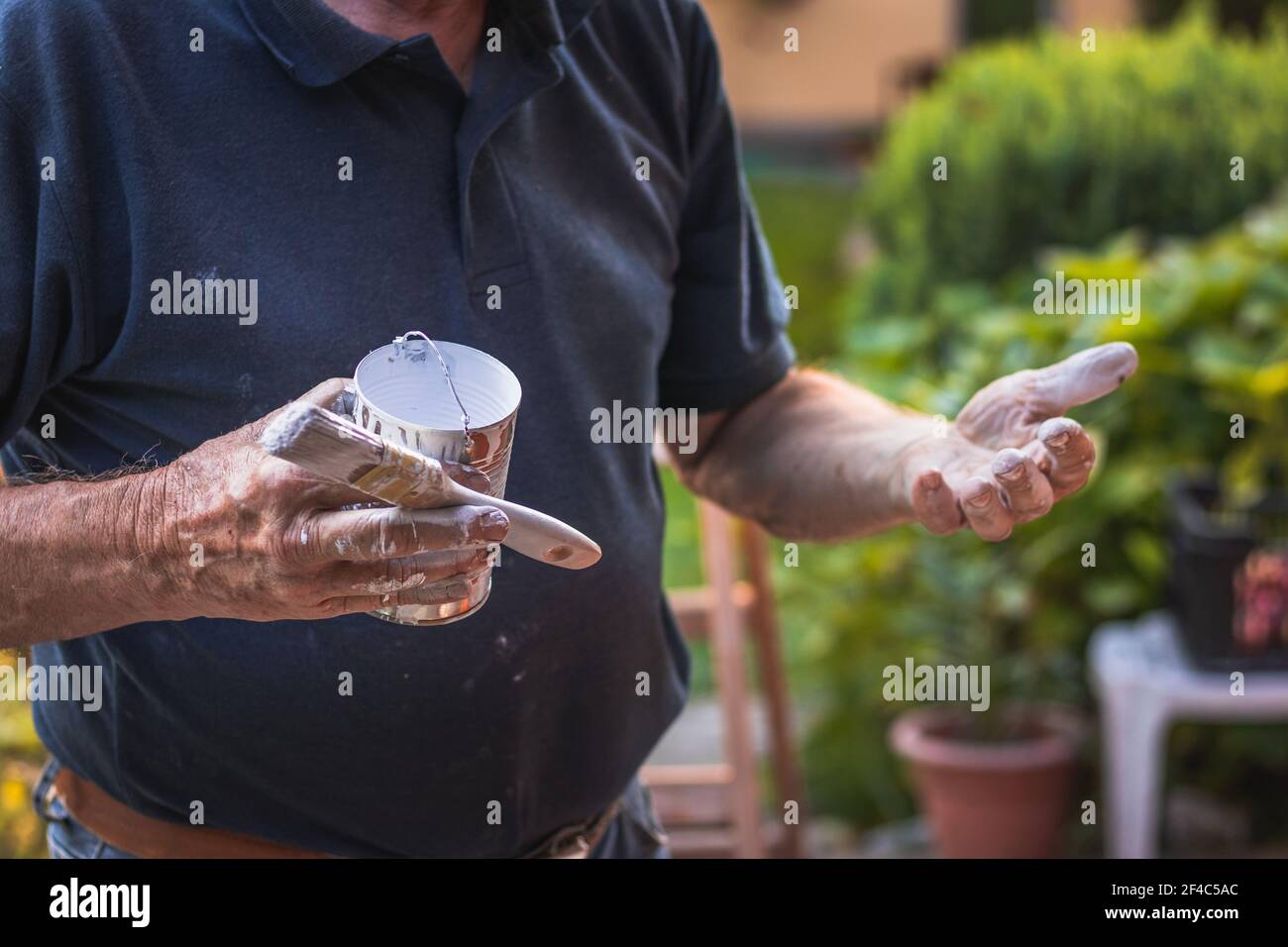 Senior craftsperson has a dirty hands after painting. Old man holding paintbrush. Stock Photo