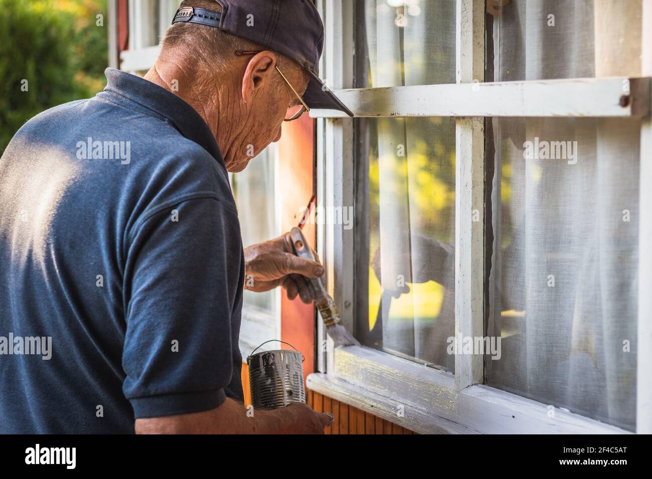 Senior craftsperson is painting house exterior. Home improvement. Old man repairing window frame. Stock Photo