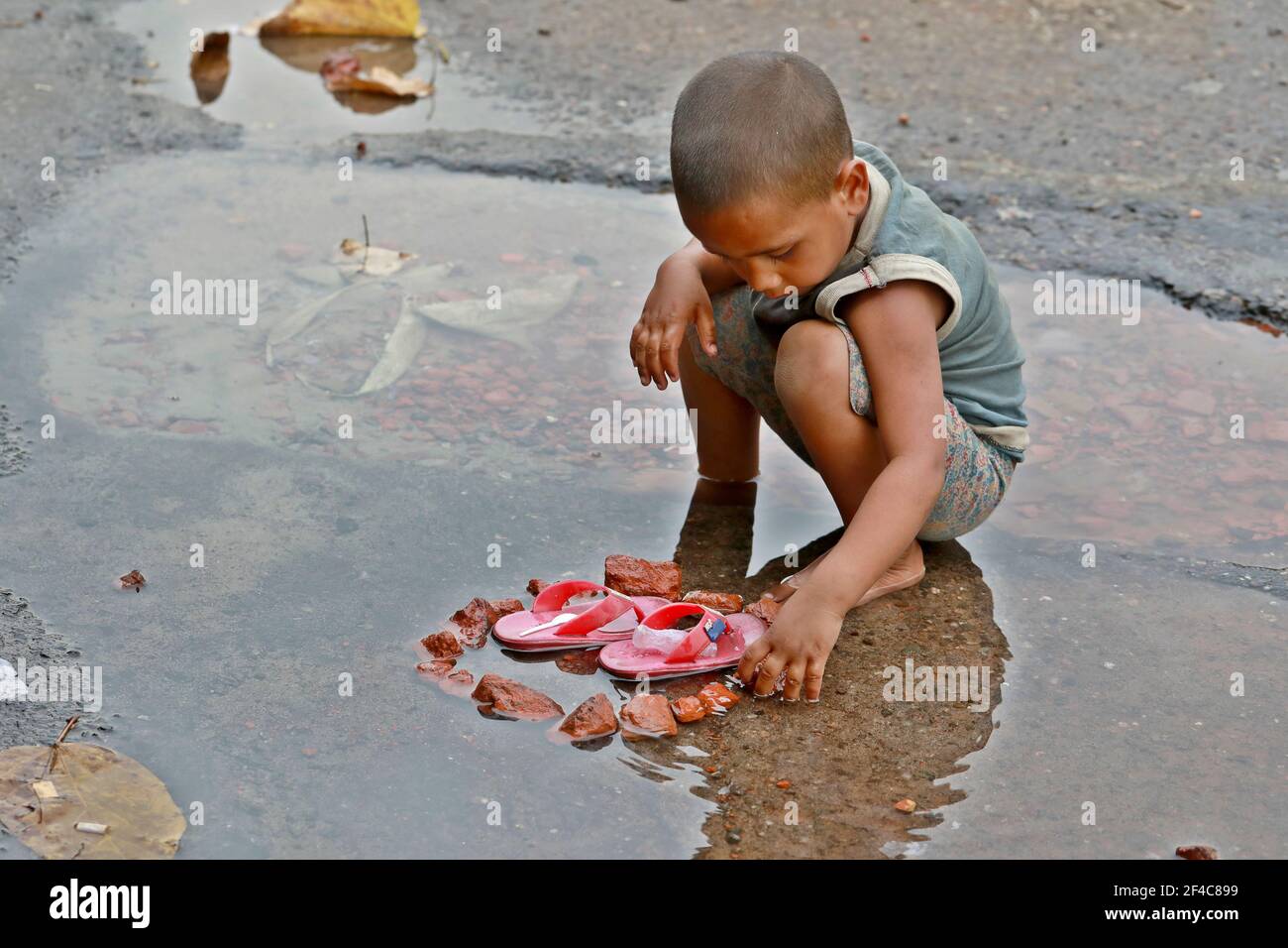 Dhaka, Bangladesh - March 20, 2021: A street child is playing in the frozen water in the Dhaka University area, Dhaka, Bangladesh. Stock Photo