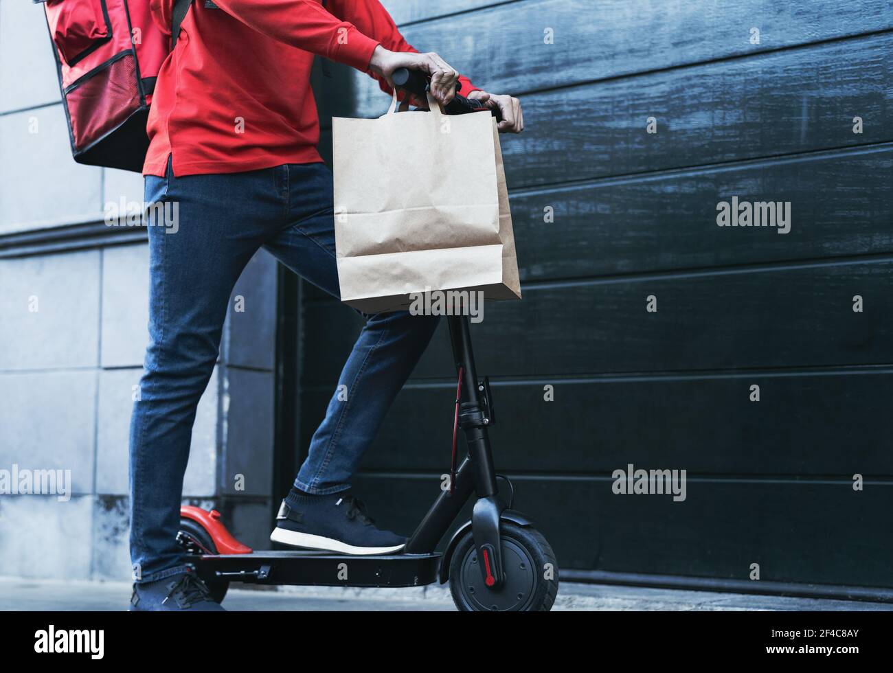 Rider man delivering meal to customers house with electric scooter - Ecological fast delivery food concept - Focus on trousers Stock Photo