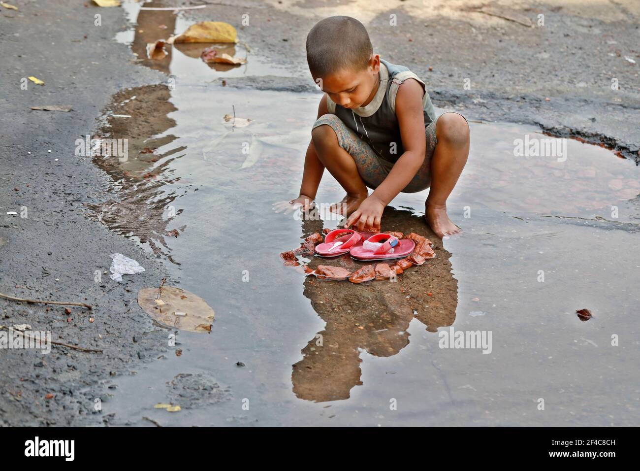 Dhaka, Bangladesh - March 20, 2021: A street child is playing in the frozen water in the Dhaka University area, Dhaka, Bangladesh. Stock Photo