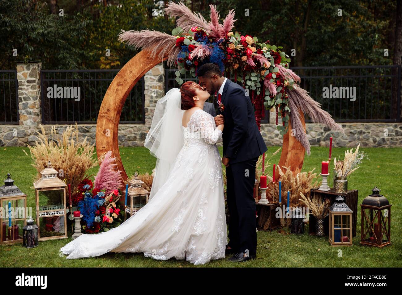 https://c8.alamy.com/comp/2F4CB8E/beautiful-white-woman-with-charming-african-american-man-stand-near-decorated-arch-adorable-couple-on-wedding-ceremony-attractive-groom-kiss-lovely-2F4CB8E.jpg