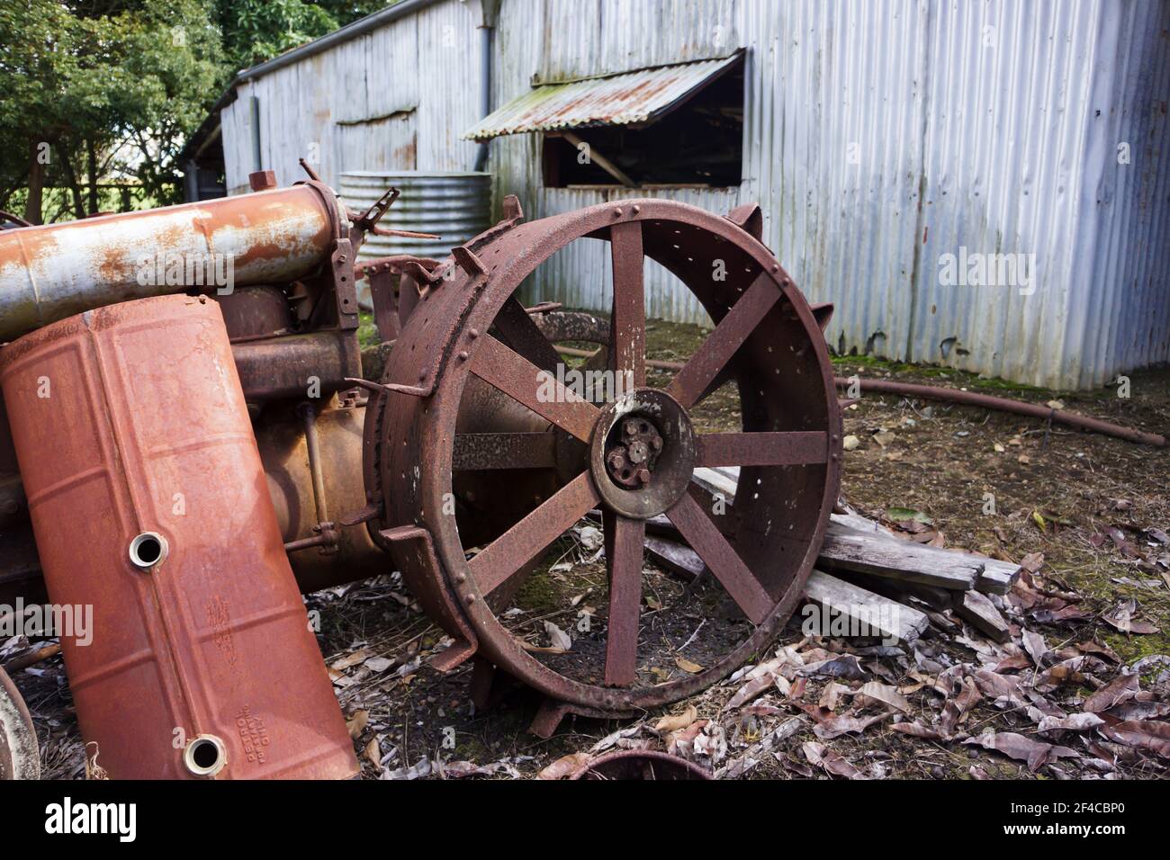 Early farm machinery discarded behind a corrugated iron shed with parts of an old tractor and fuel tank used by early settlers. Stock Photo
