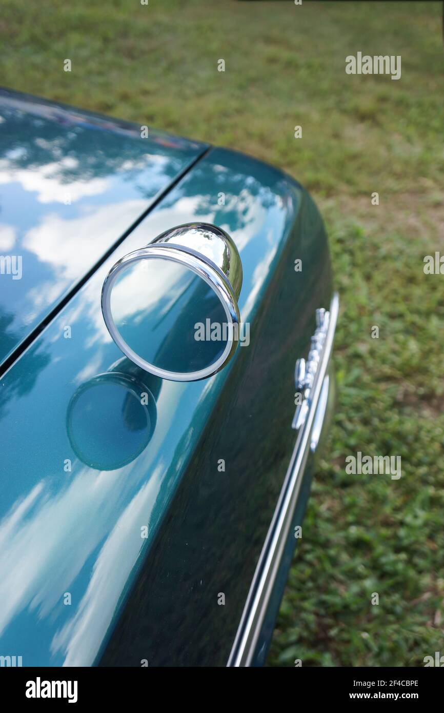 A rear view mirror set on the mudguard of a green classic car with reflections of the sky in the highly polished metal. Stock Photo