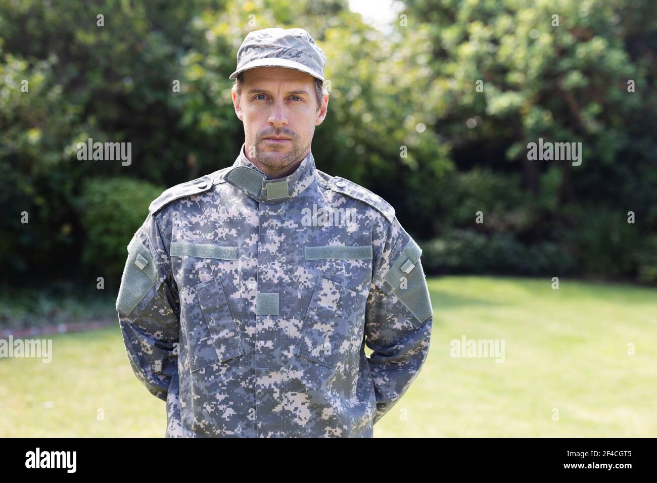 Portrait of caucasian male soldier wearing camo fatigues and cap standing in garden Stock Photo