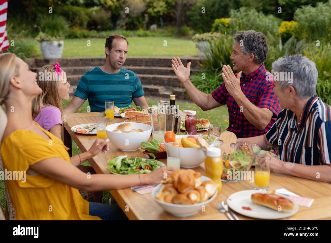 Caucasian senior man sitting at table talking with family having meal in garden Stock Photo