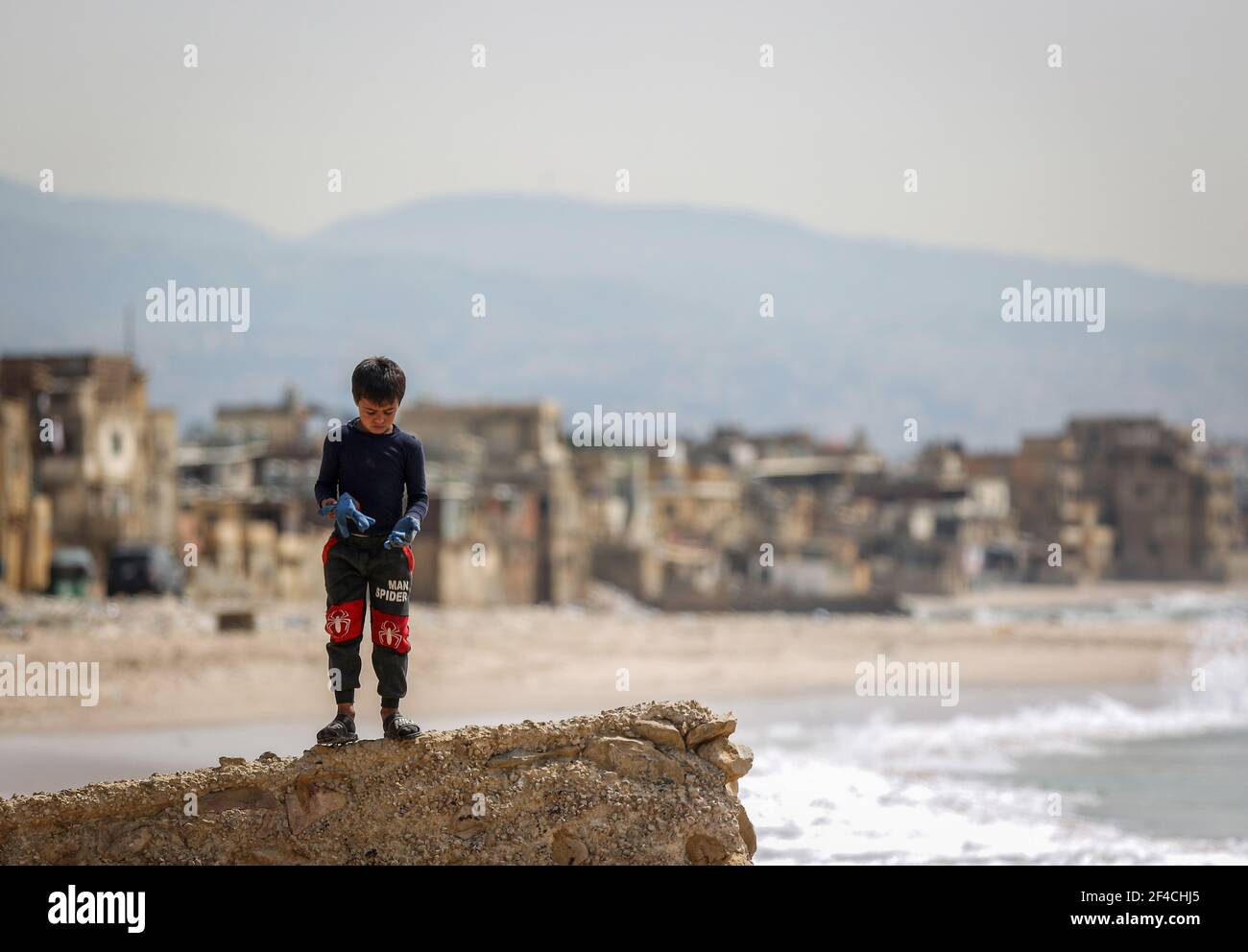 20 March 2021, Lebanon, Beirut: A boy takes off gloves after cleaning the coast of San Simon at Ouzai area  following the leakage of an Israeli oil tanker last month. Photo: Marwan Naamani/dpa Stock Photo