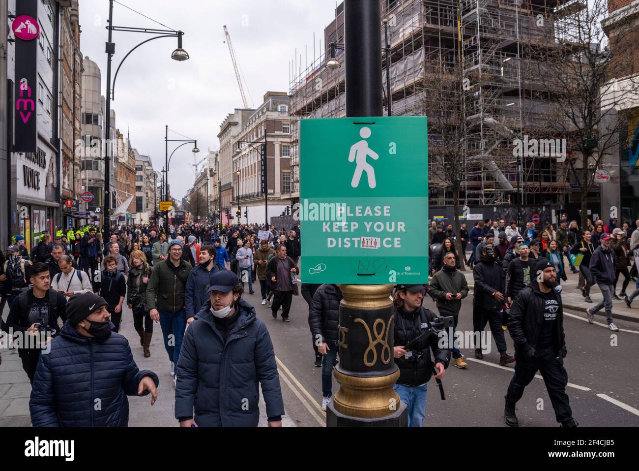Westminster, London, UK. 20th Mar, 2021. An anti-lockdown protest march is underway in London. Protesters gathered in Hyde Park before marching through the park and heading out, blocking traffic in Park Lane and beyond. Crowd passing along Oxford Street, and social distancing sign Stock Photo