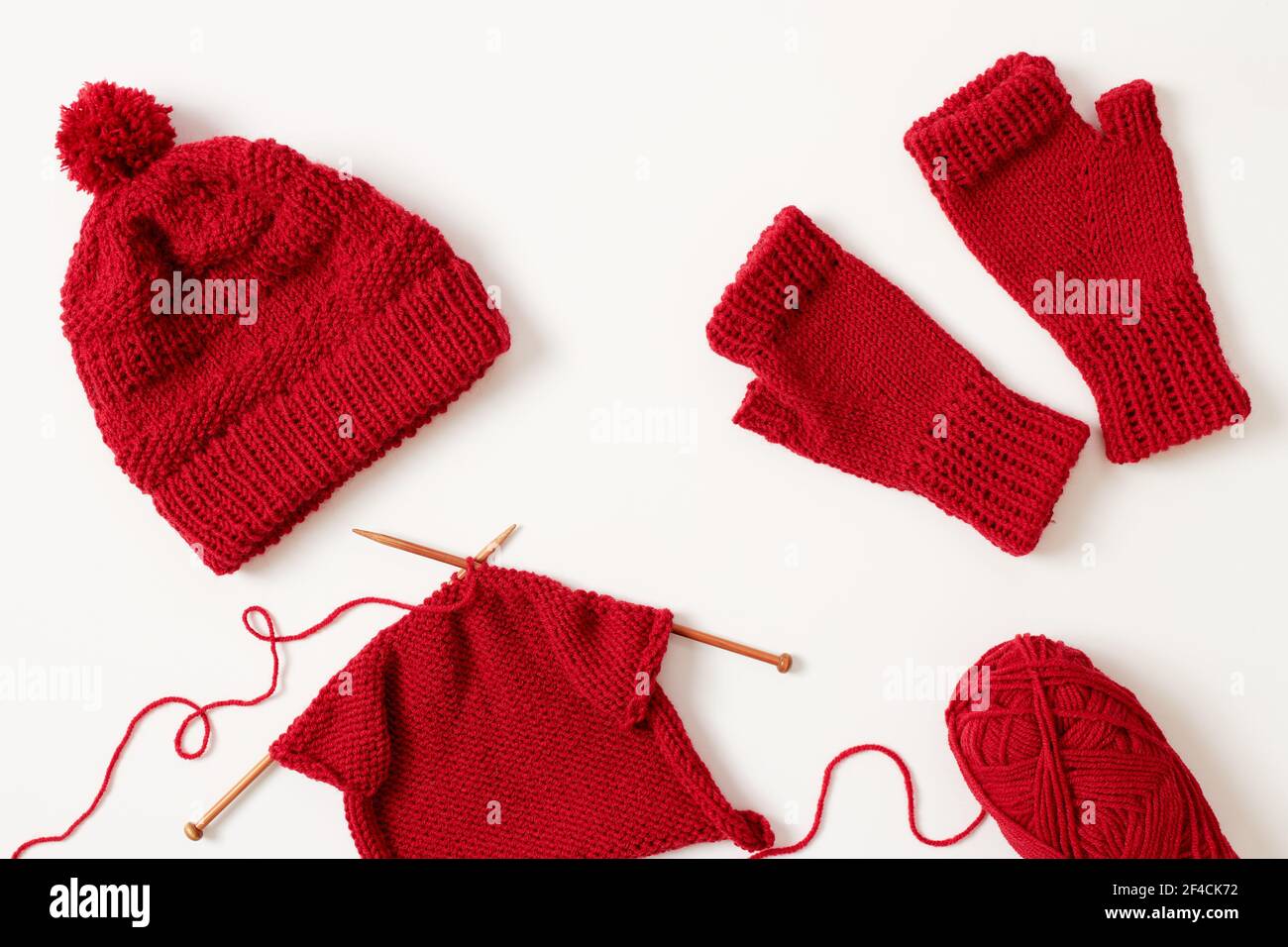 Knitting project in progress. Winter hat and mittens knitted with red yarn on white background. Stock Photo
