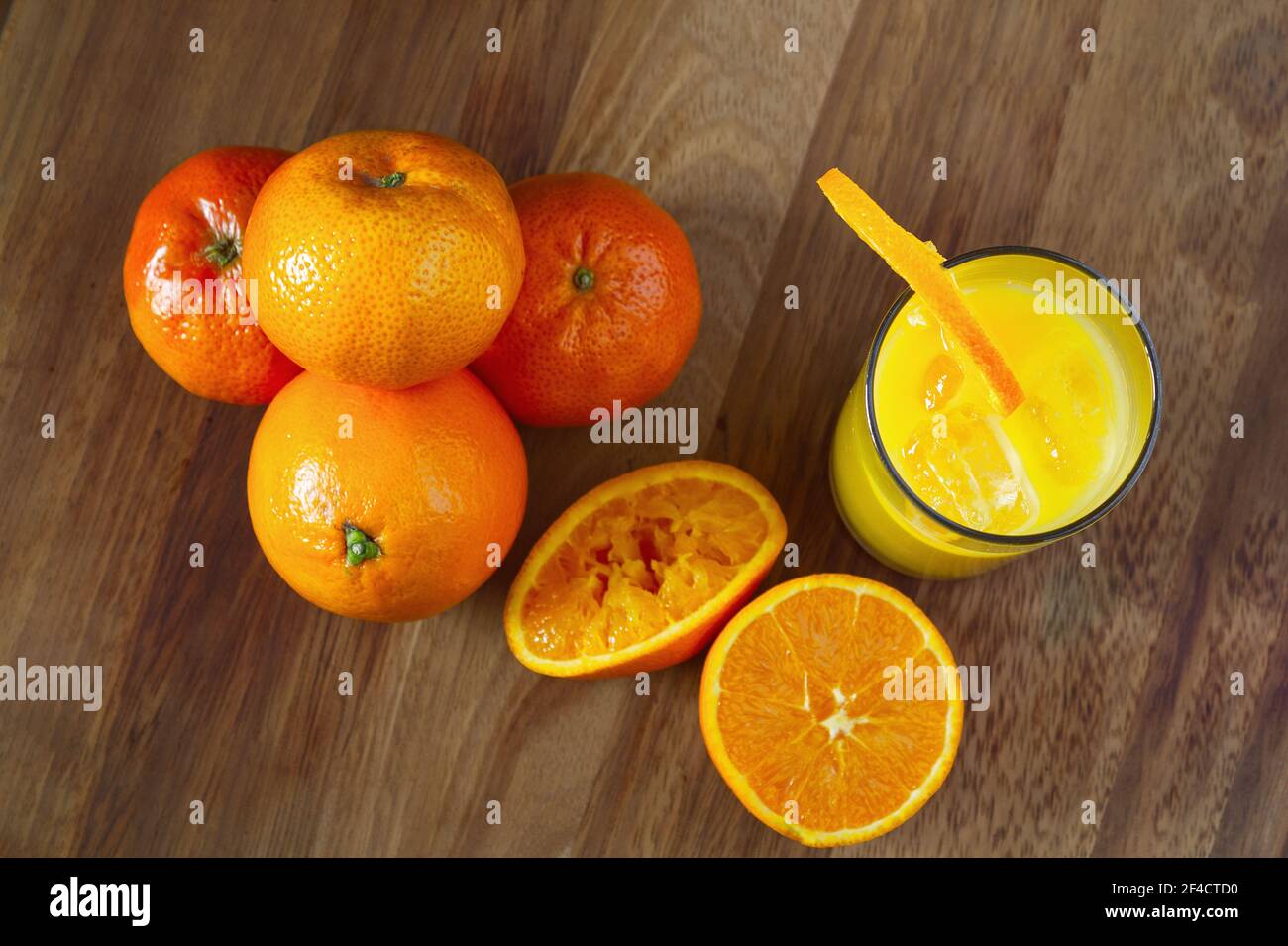 Viewed from above Orange Juice and a pile of Oranges to the left. Orange Half and a Squeezed Oranges in the Centre. placed on a wooded board. Stock Photo